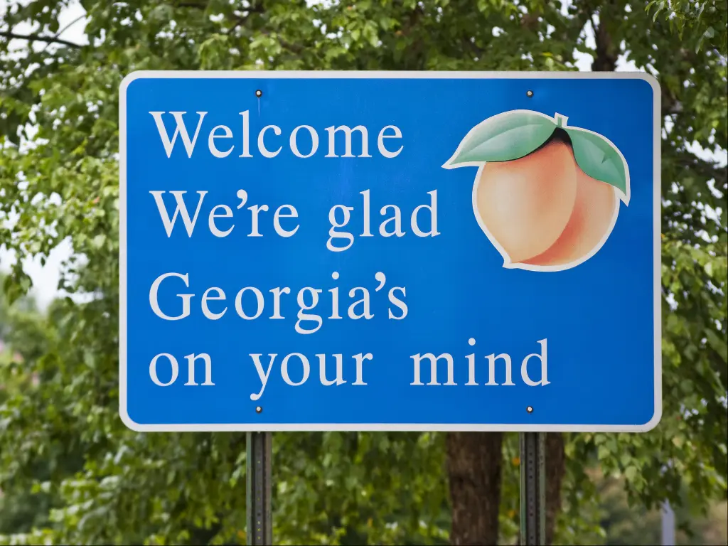 A blue welcome sign as you enter the state of Georgia. Reads: "Welcome we're glad Georgia's on your mind", with a peach