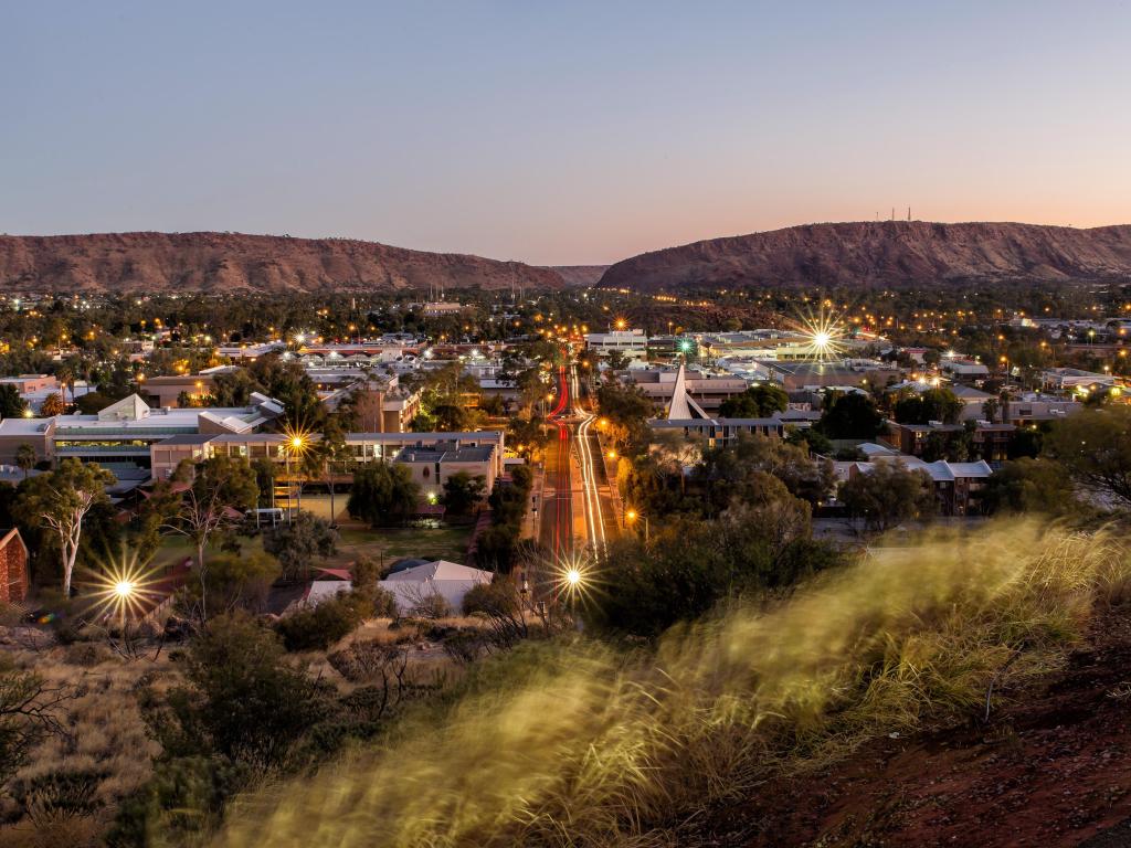 Aerial view of Alice Springs with low evening light, lights across the city and mountains in the background
