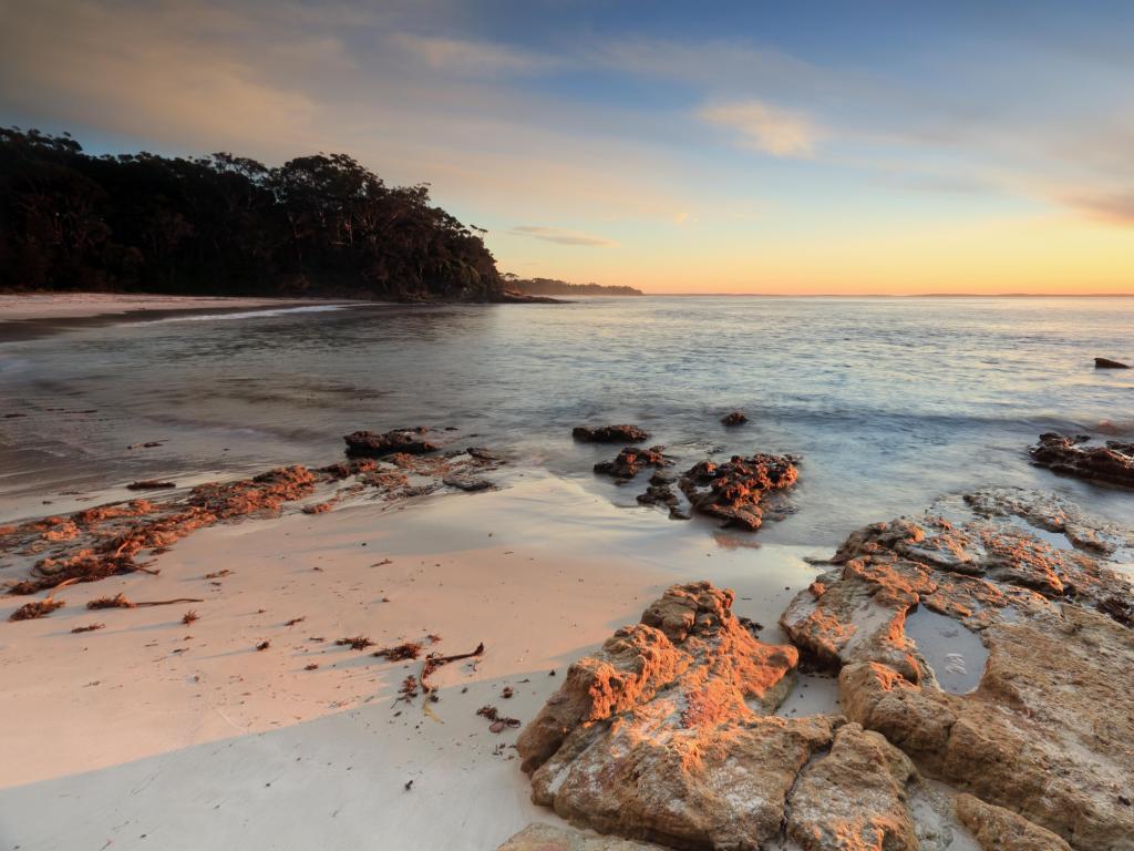 Beautiful warm golden sunlight streaming onto a sandy beach with still water and low cliffs rising around the bay