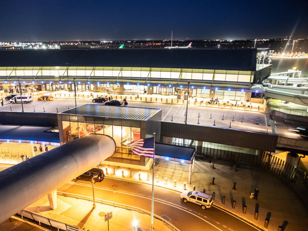 Top view of the entrance of John F Kennedy airport during the night with lights on. Some cars are on the road.