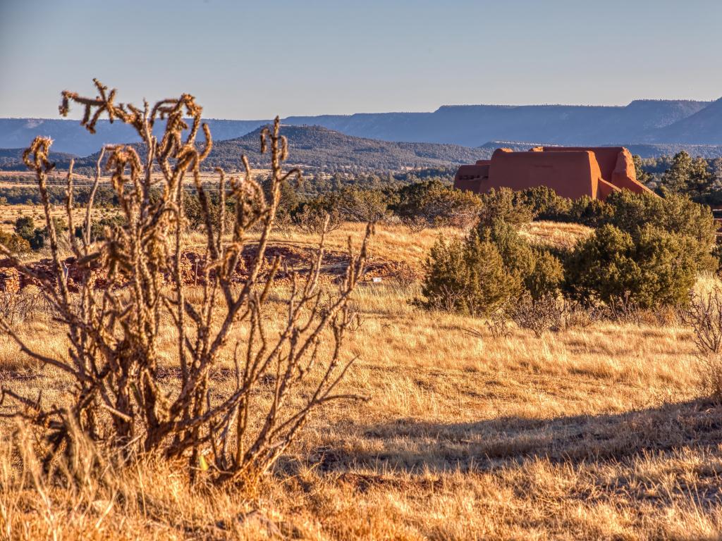 Pecos National Historic Park, Santa Fe, New Mexico, USA with plants, grasses and bushes in the foreground and a buildings and hills in the distance taken on a sunny day.