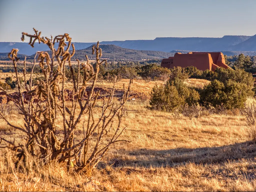 Pecos National Historic Park, Santa Fe, New Mexico, USA with plants, grasses and bushes in the foreground and a buildings and hills in the distance taken on a sunny day.
