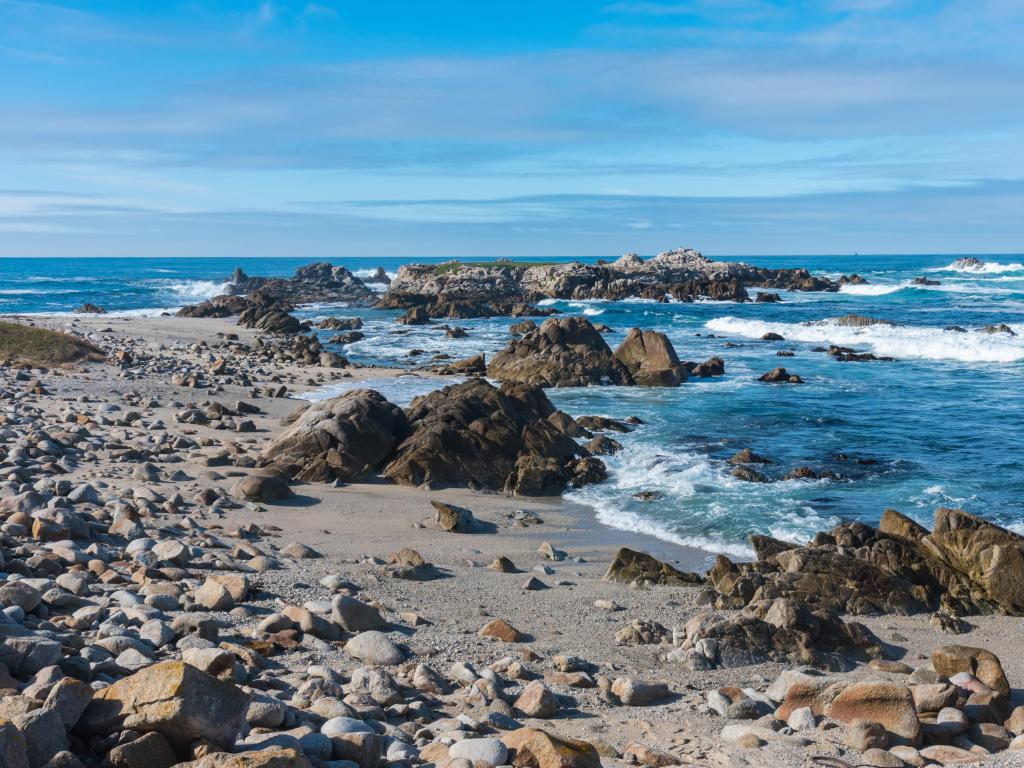 Monterey Bay, California with waves crashing against the rocky shoreline and a bright blue sky.