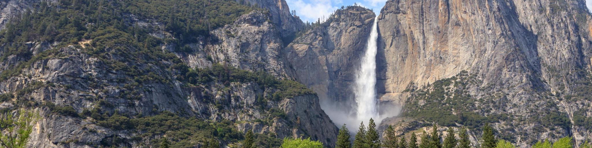 View of Bridalveil Fall with forests in the foreground, and blue skies overhead