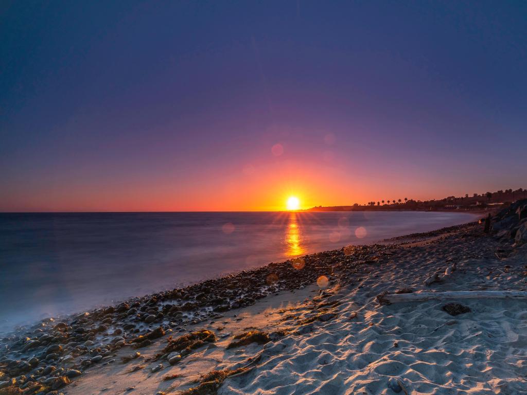 Setting sun reflecting on water with white sand in the foreground