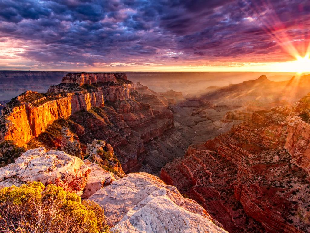 Impressive depth of the Grand Canyon in contrast to bright sunshine emerging underneath purple and pink clouds