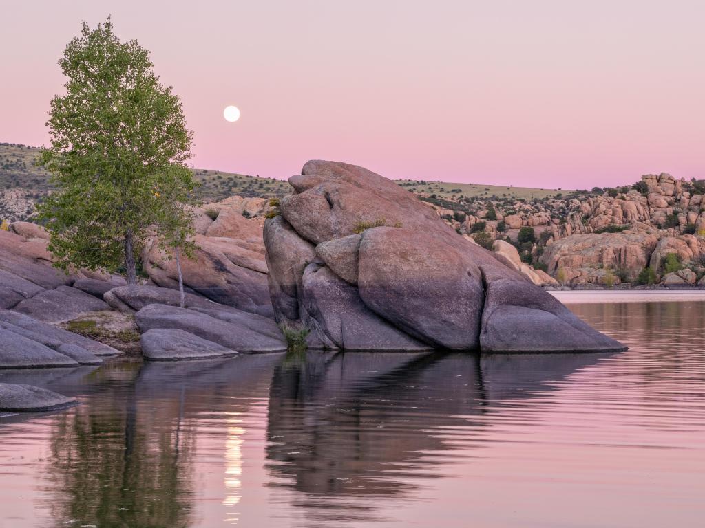Watson Lake, Prescott, Arizona, USA taken with a moonrise in the distance and boulders in the lake in the foreground. 