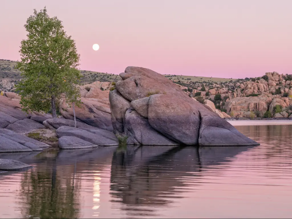 Watson Lake, Prescott, Arizona, USA taken with a moonrise in the distance and boulders in the lake in the foreground. 