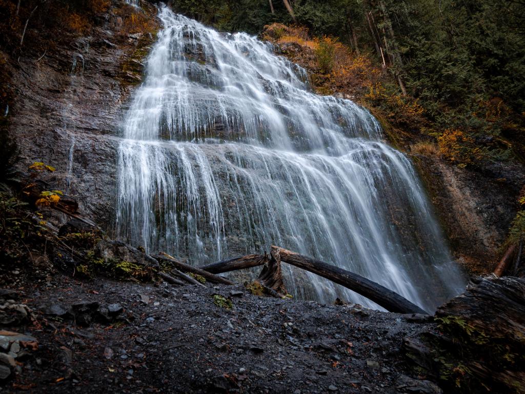 Beautiful waterfalls cascading over a stone wall with autumnal foliage surrounding it