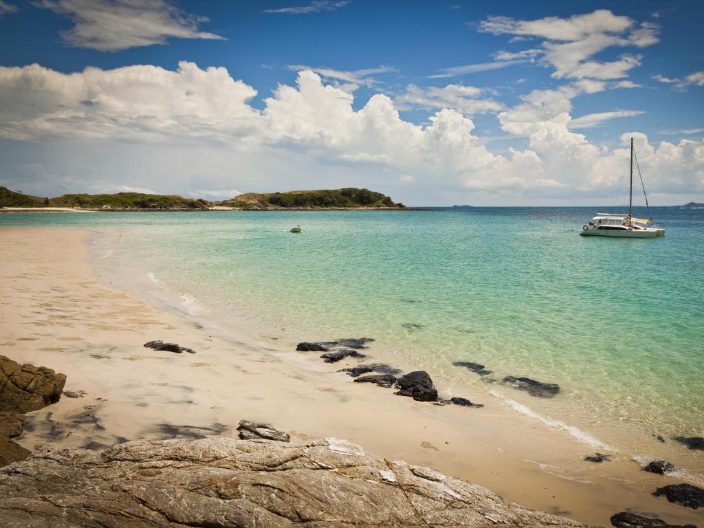 Keppel Island, Queensland, Australia with golden sand beside a turquoise ocean with a boat in the distance. 