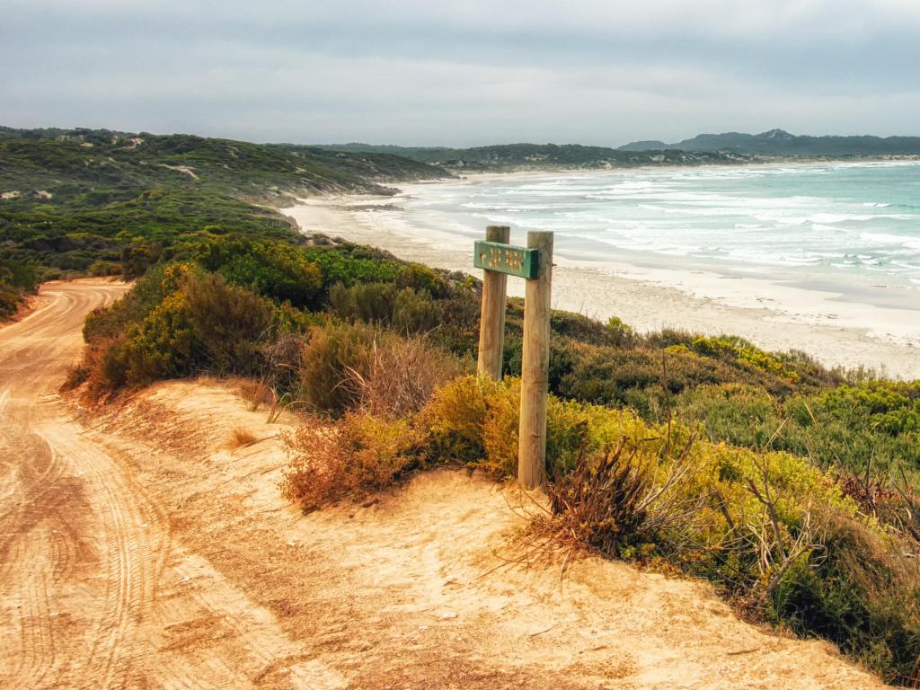 Port Lincoln, South Australia with a sign leading to a yellow path, shrubs and the sea leading into the distance. 