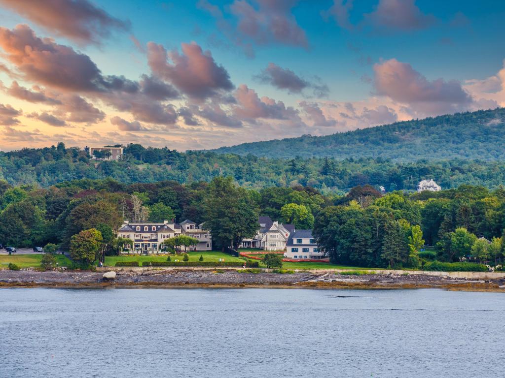 Bar Harbor, Maine, USA with classic old hotels and bed and breakfast houses on the coast of Maine, forest mountains in the distance and the ocean in the foreground.