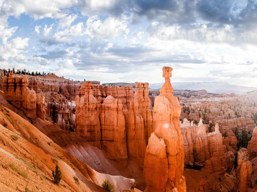 Bryce Canyon National Park, Utah, USA with a scenic panoramic view of famous Hoodoos sandstone formations in Bryce Canyon National Park illuminated in beautiful golden morning light at sunrise with dramatic sky and blue sky.