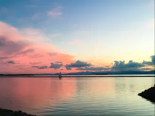 Lake Champlain in Burlington, Vermont, USA with a sailboat at sunset on Lake Champlain in Burlington, Vermont. The vibrant pink sky transitions to a cool blue in both the sky and the water.