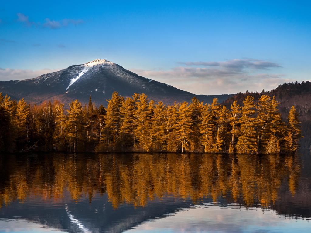 Lake Placid, Upstate New York, USA with snowy Whiteface mountain in the background and reflections in Paradox Bay in the foreground, taken during the fall with oranges trees between the two. 