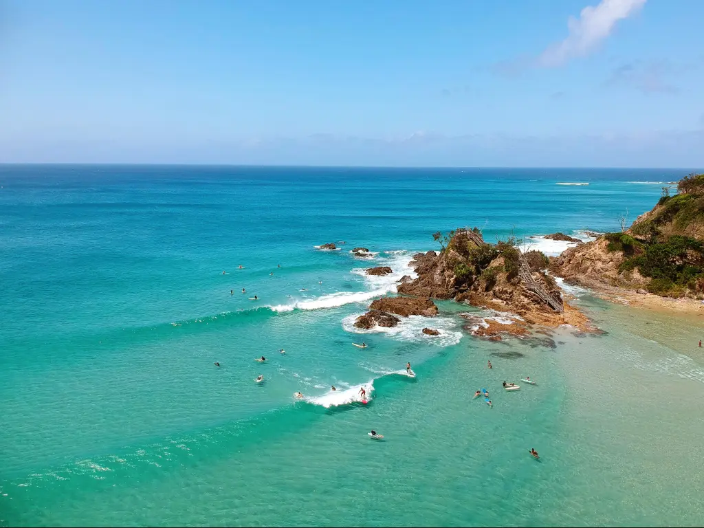 Byron Bay, Australia with surfers riding the waves in the clear water and rock formations into the distance. 