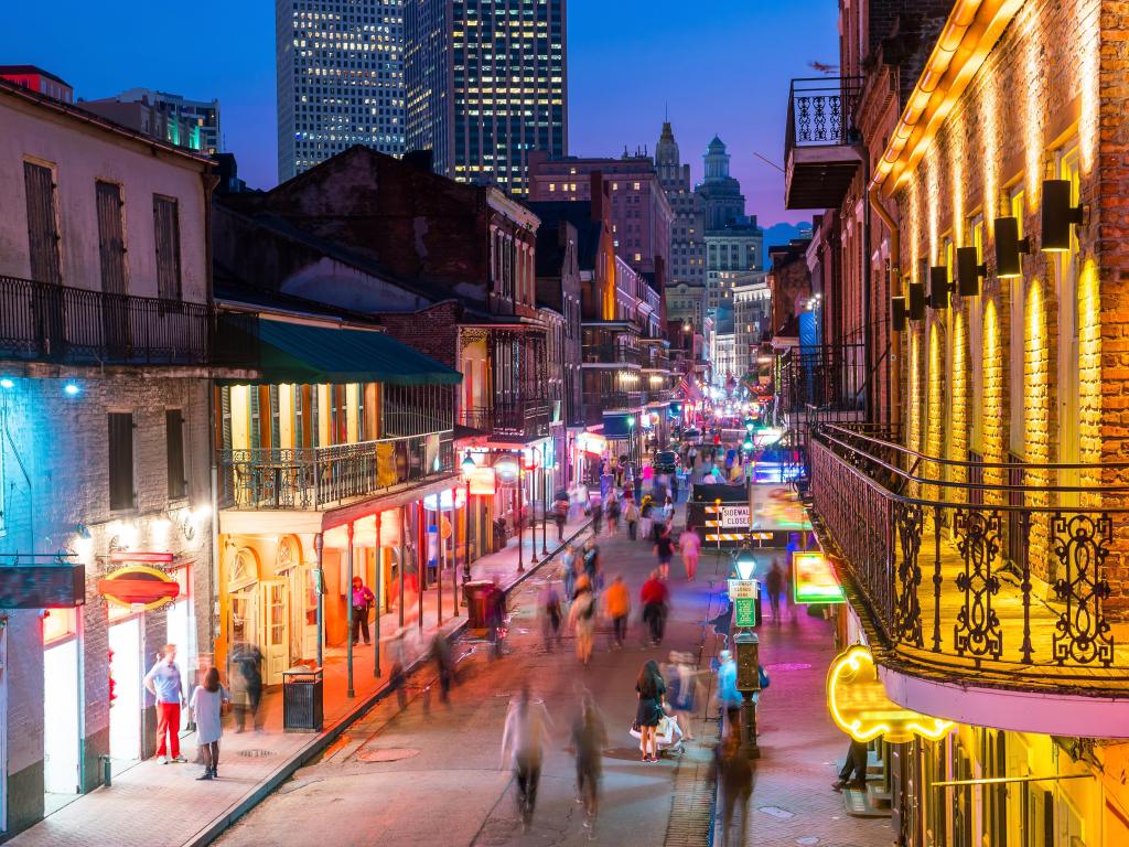 New Orleans, showing the pubs and bars with neon lights in the French Quarter at night with people walking in the streets and a skyscraper in the background. 