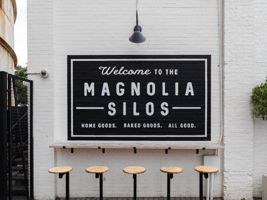 Famous Magnolia Silos in Waco, a seating area with stools facing a white brick wall with a black sign that says 