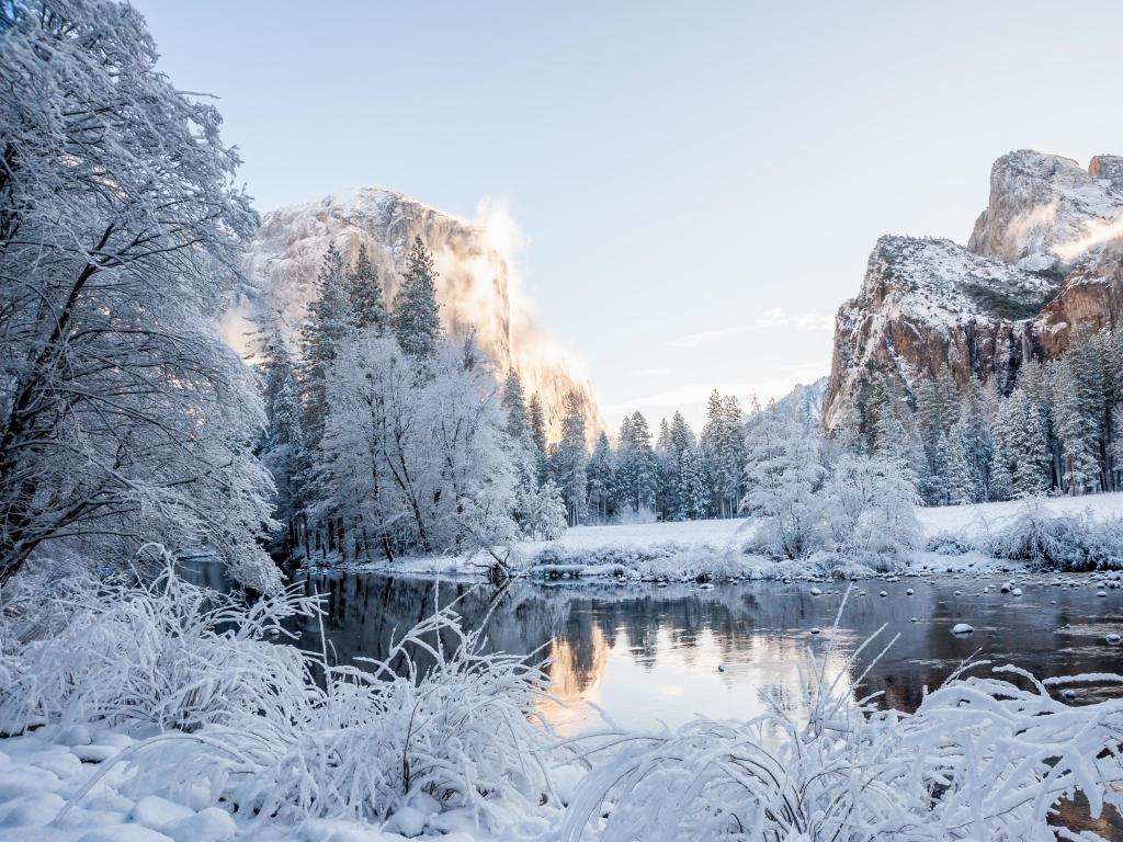 Clear water reflecting snow covered trees with rocky cliffs