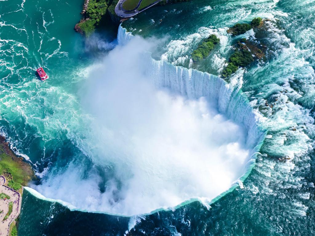View of falls from above with bright blue river water and white spray rising from pool below