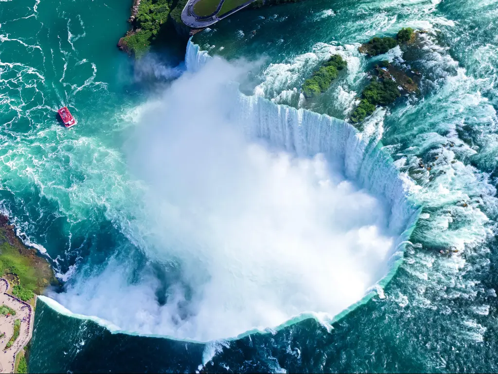 View of falls from above with bright blue river water and white spray rising from pool below