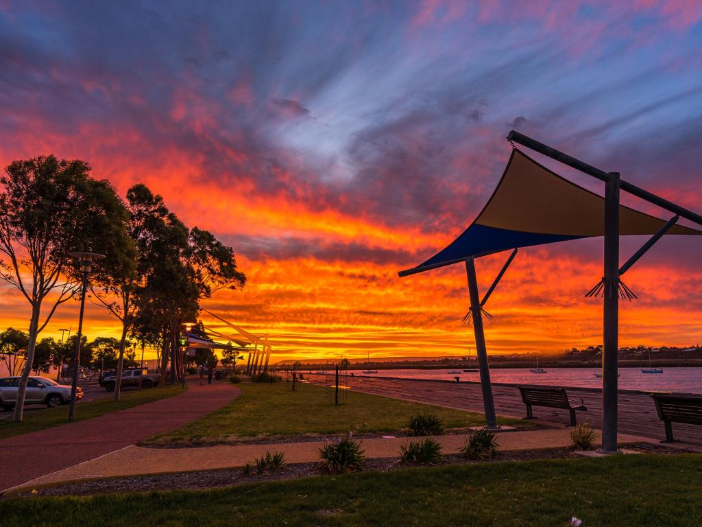 Vibrant red and orange sunset over calm river with benches and sunshades