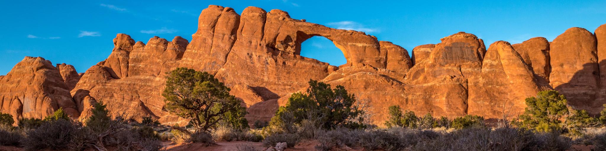 Bright sunlight illuminating the beautiful Skyline Arch sandstone rock formation at golden hour, Arches National Park, Moab, Utah