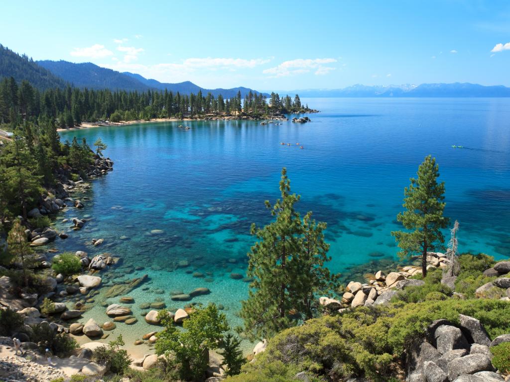 Lake Tahoe on a sunny day. The blue sky almost merges with the blue waters. There are some trees on the lakeshore. 