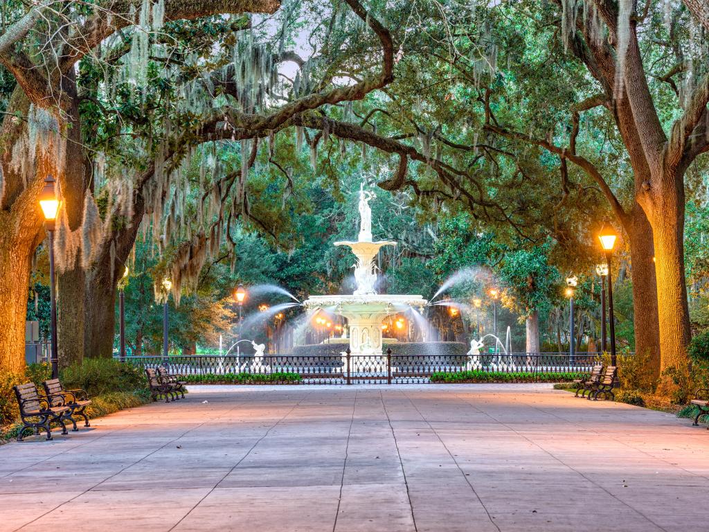 Savannah, Georgia, USA at Forsyth Park at early evening with street lights on, trees lining the path and the water fountain in the distance. 