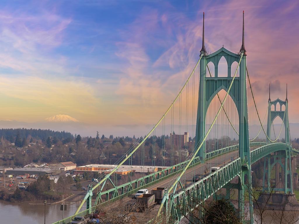 Green metal bridge across river with snow capped volcano in the distance