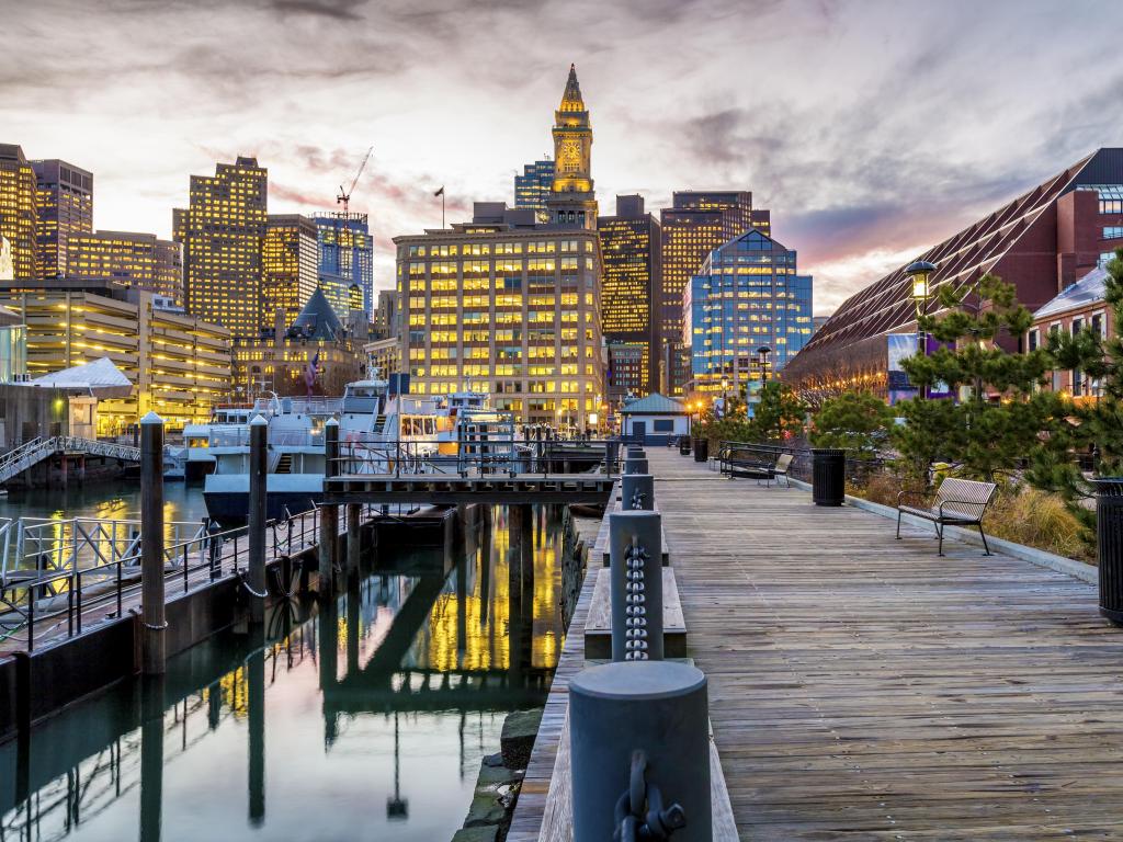 Boston Harbor downtown at dusk, with buildings lit up and reflections in the water