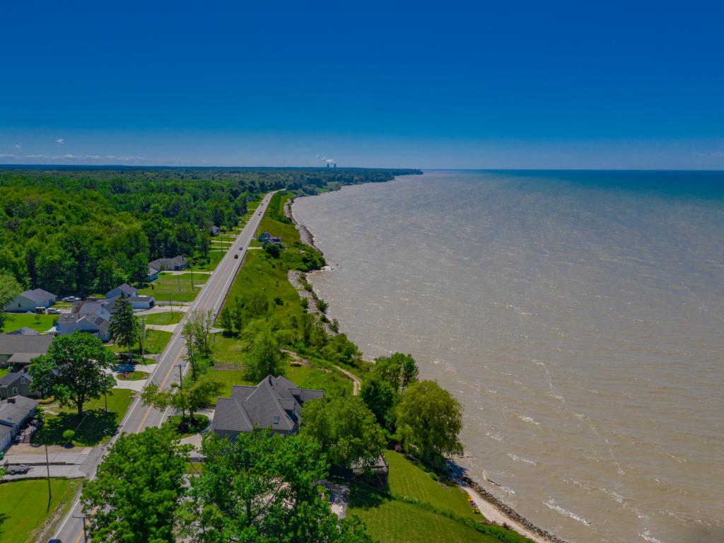 An aerial view of green forest-like trees and Lakeside road along Lake Erie Coastline in a good weather