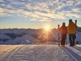 Two people holding skis and watching the sun set over the mountains at Ischgl