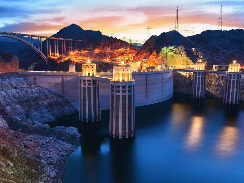 Hoover Dam in Boulder, Nevada, USA taken as an evening view of the Hoover Dam with pretty lights and calm water in the foreground.