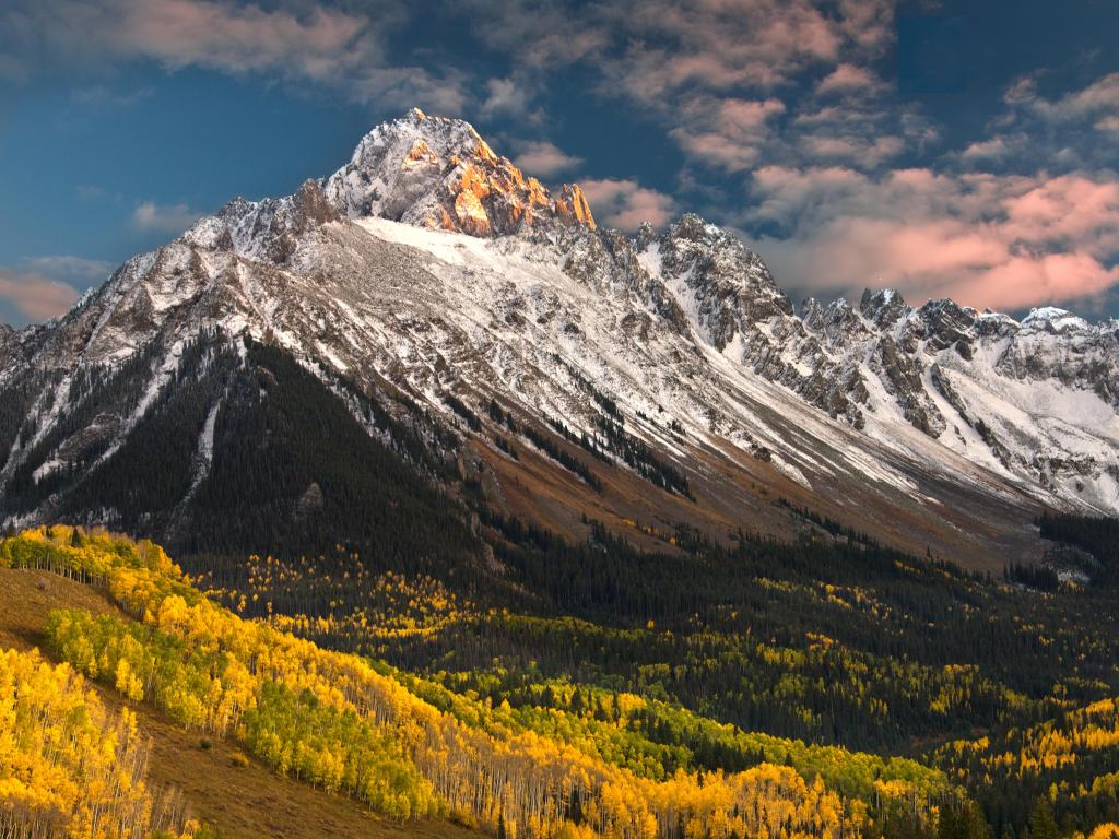 Rocky mountain with snow in places, with trees lower down lit up green and gold