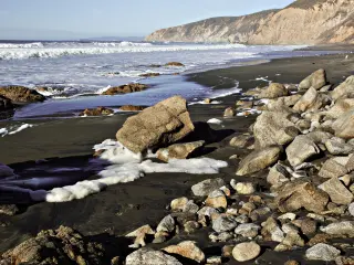 Rocks dotted across McClures Beach with cliffs in background and crashing waves