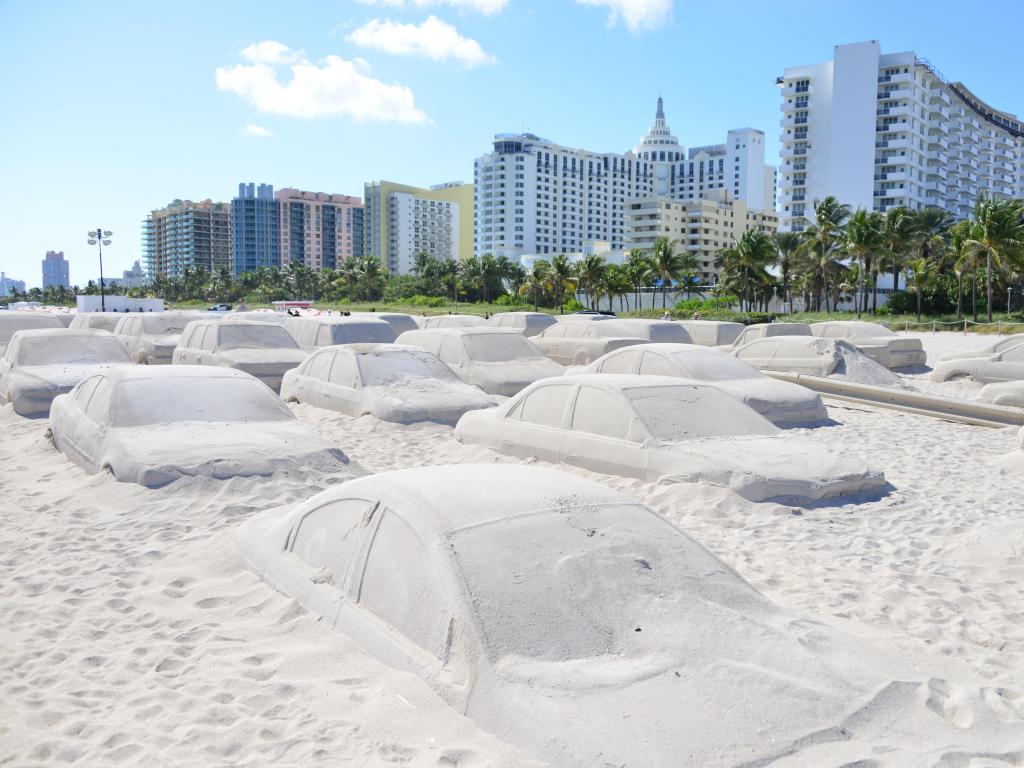 Cars made out of sand on the beach on a sunny day. Most the car hoods can be seen