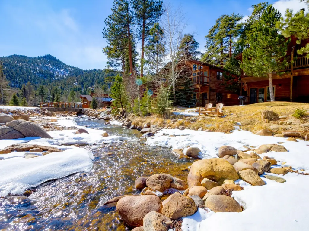 Beautiful wooden lodge by crystal-clear waters of the river with mountains in the background