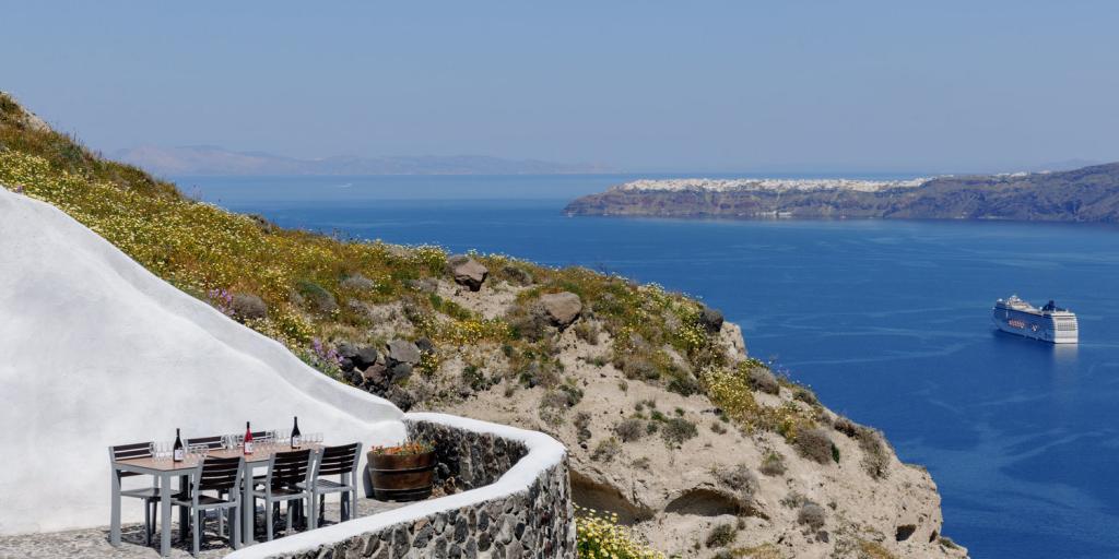 A table with wine bottles on top looks over the cobalt blue sea in Santorini