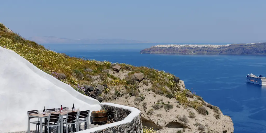 A table with wine bottles on top looks over the cobalt blue sea in Santorini