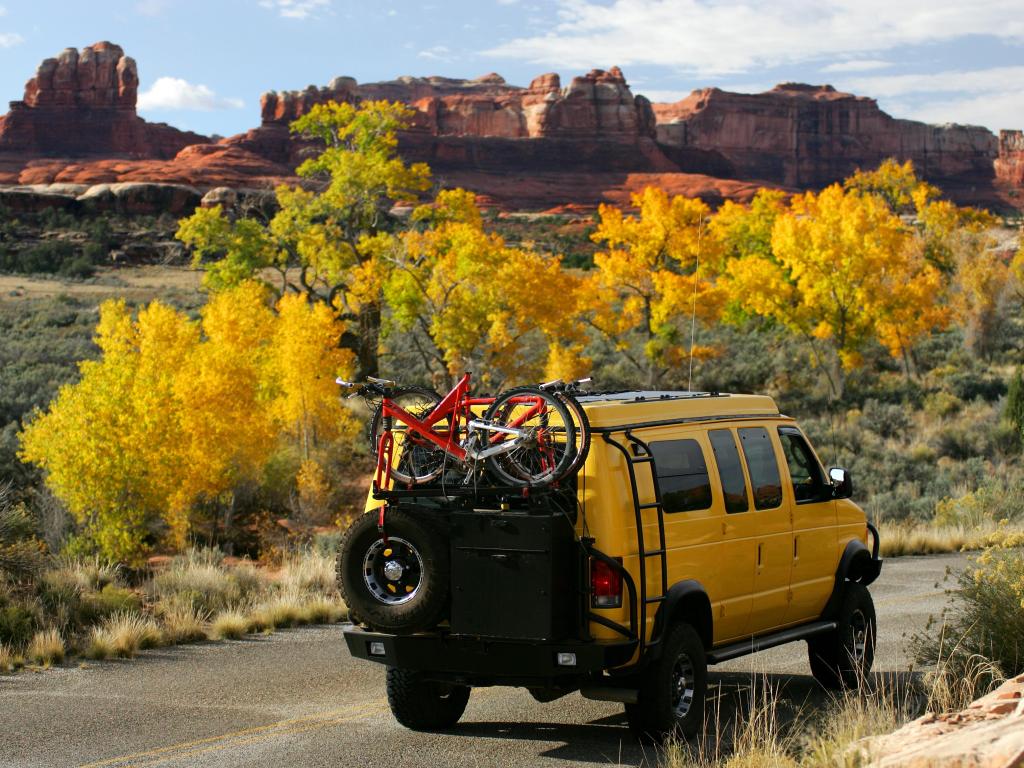 A yellow 4 Wheel Drive vehicle driving through Canyonlands National Park, with red rocks behind and yellow foliage