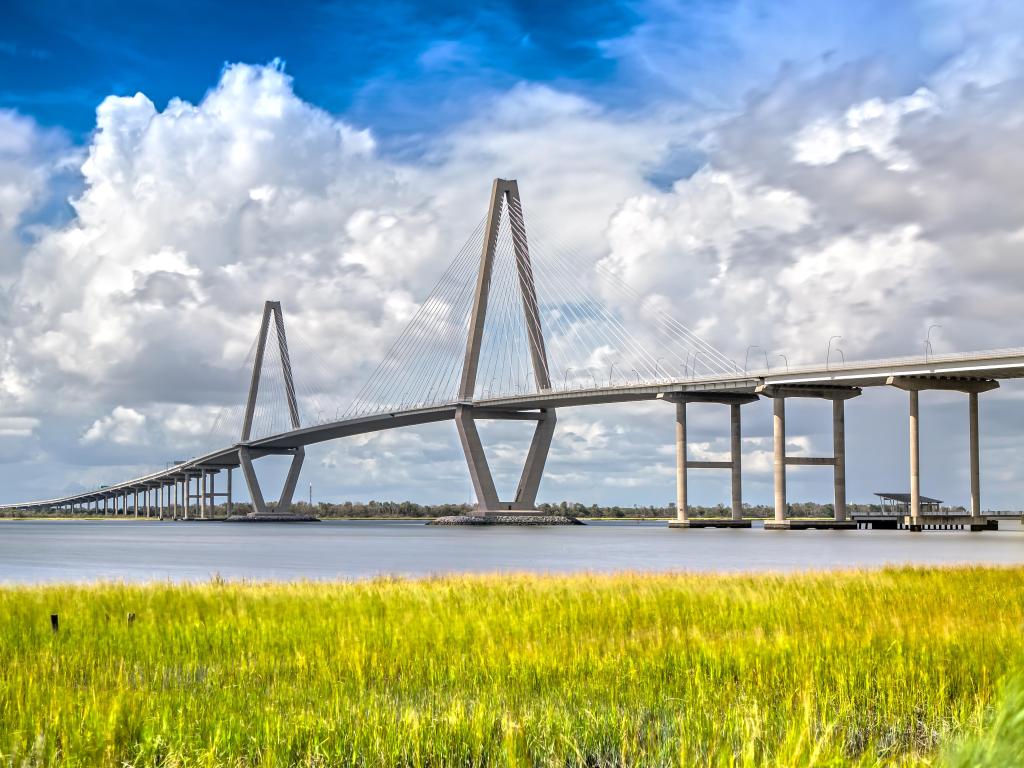 Full view of Arthur Ravenel Bridge in Charleston, against blue and cloudy skies with grasslands in the foreground