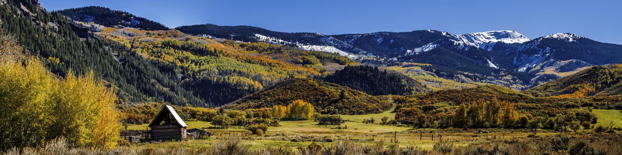 Panorama showing landscape with brilliant fall colors along road to Capitol Peak near Aspen Colorado on sunny autumn afternoon