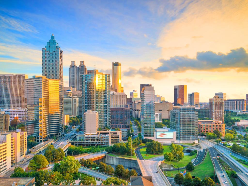 High rise buildings lit up in golden sunset light, with green space and highways at ground level