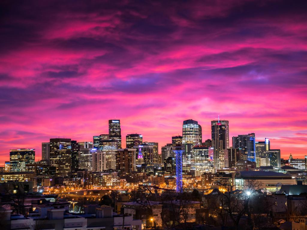Denver, USA downtown at sunrise under a pink sky with the city buildings lit up.