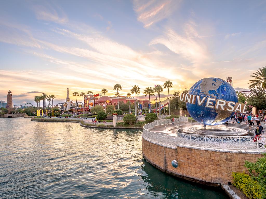 Orlando, Florida, USA with the Universal Studios globe located at the entrance to the theme park in the foreground, surrounded by water and the park in the distance taken at sunset.