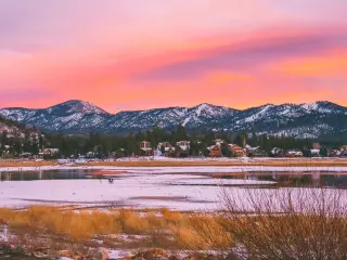 View of the lake during a pink sunset with snow on the mountains in the background
