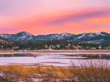 View of the lake during a pink sunset with snow on the mountains in the background