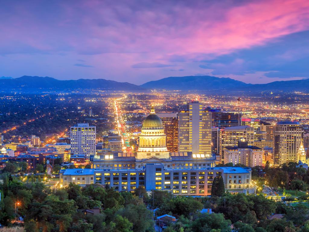 Salt Lake City, Utah, USA with the city skyline at night, mountains in the distance and trees in the foreground.