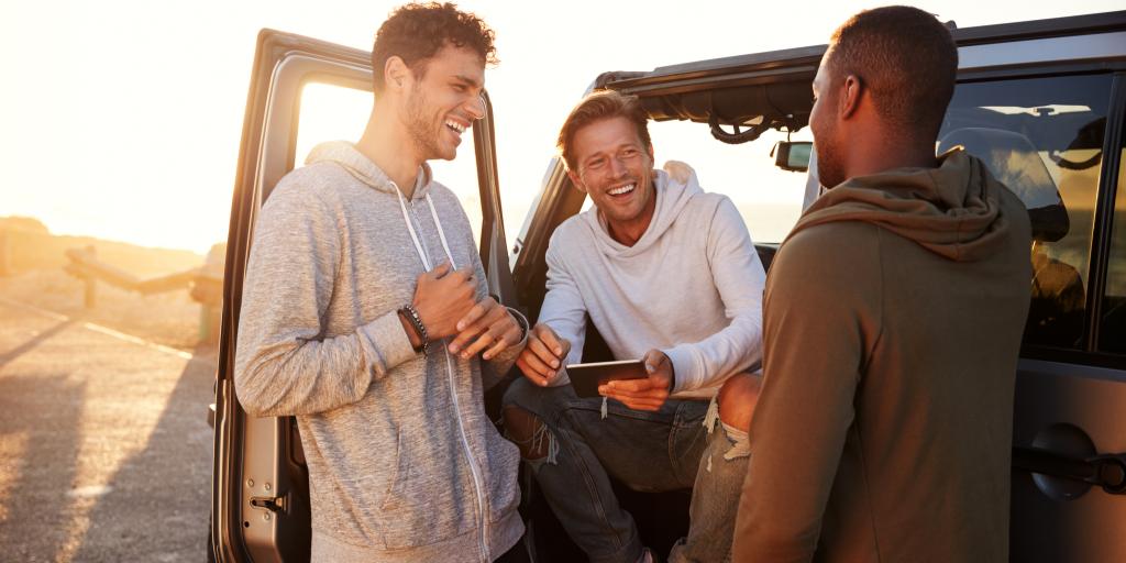 Three male friends laughing with each other on a road trip